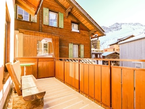 Eine Holzchalet mit Balkon, einer Bank und Blick auf schneebedeckte Berge.