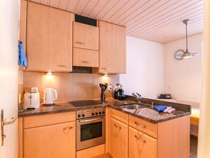 Eine kleine Küche mit Holzausstattung, einem Bosch-Backofen, einer Kaffeemaschine und einem Spülbecken.