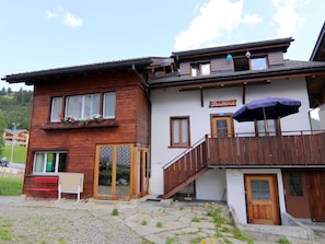 Ein zweistöckiges Gebäude mit Holzfassade, einem Balkon mit blauem Sonnenschirm und einem Schild mit dem Schriftzug 'Pautina'.