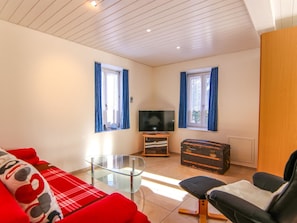 Ein Wohnzimmer mit Glastisch, rotem Sofa, schwarzem Sessel, Fernseher und Holzschrank.