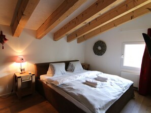 A bedroom with a bed, a nightstand, a lamp, a wall decoration, and a window. - Rothornblick 65 by Arosa Holiday Appartement/Fewo, Dusche und Bad, WC, 6-Bettwoh by Interhome (Arosa)