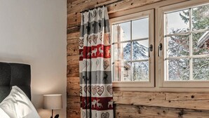 A bedroom with a bed, a nightstand, a lamp, a window with a view of a mountain, and wooden paneling. - Alpslodge Amelia Appartement/Fewo, Bad, WC, Terrasse by Interhome (Arosa)