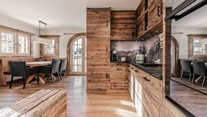 A modern kitchen with wooden accents, a dining area with a wooden bench, and a large window. - Alpslodge Amelia Appartement/Fewo, Bad, WC, Terrasse by Interhome (Arosa)