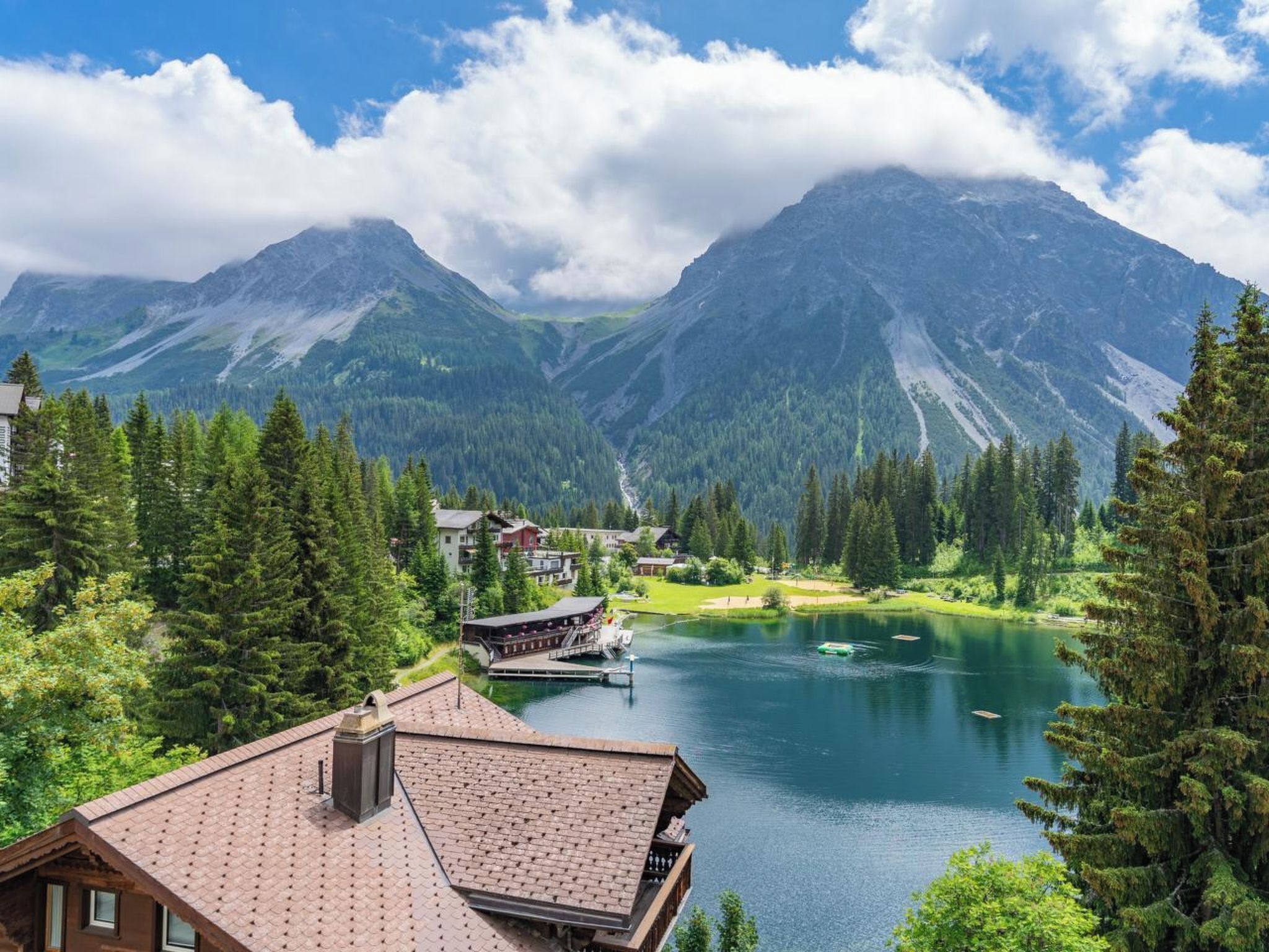 A mountain lodge with a lake view, surrounded by forest and mountains.