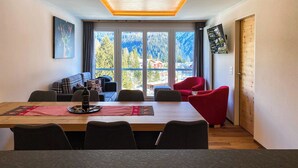 Ein modernes Zimmer mit einem großen Tisch, roten Stühlen, einer Couch und einem Fernseher an der Wand.