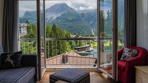 Ein Zimmer mit einem großen Glastür, das auf einen Balkon führt, ein rotes Sessel, eine Couch und ein Holztisch.
