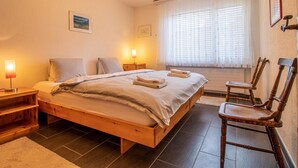 A bedroom with a wooden bed, bedside lamps, a window with blinds, and a chair. - Villa Franca U01 Appartement/Fewo,   Villa Franca UO1 by Interhome (Arosa)