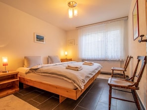 A bedroom with a wooden bed, bedside lamps, a window with blinds, and a chair. - Villa Franca U01 Appartement/Fewo,   Villa Franca UO1 by Interhome (Arosa)