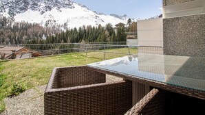 A modern outdoor seating area with a glass table and wicker chairs, overlooking a mountainous landscape. - Villa Franca U01 Appartement/Fewo,   Villa Franca UO1 by Interhome (Arosa)