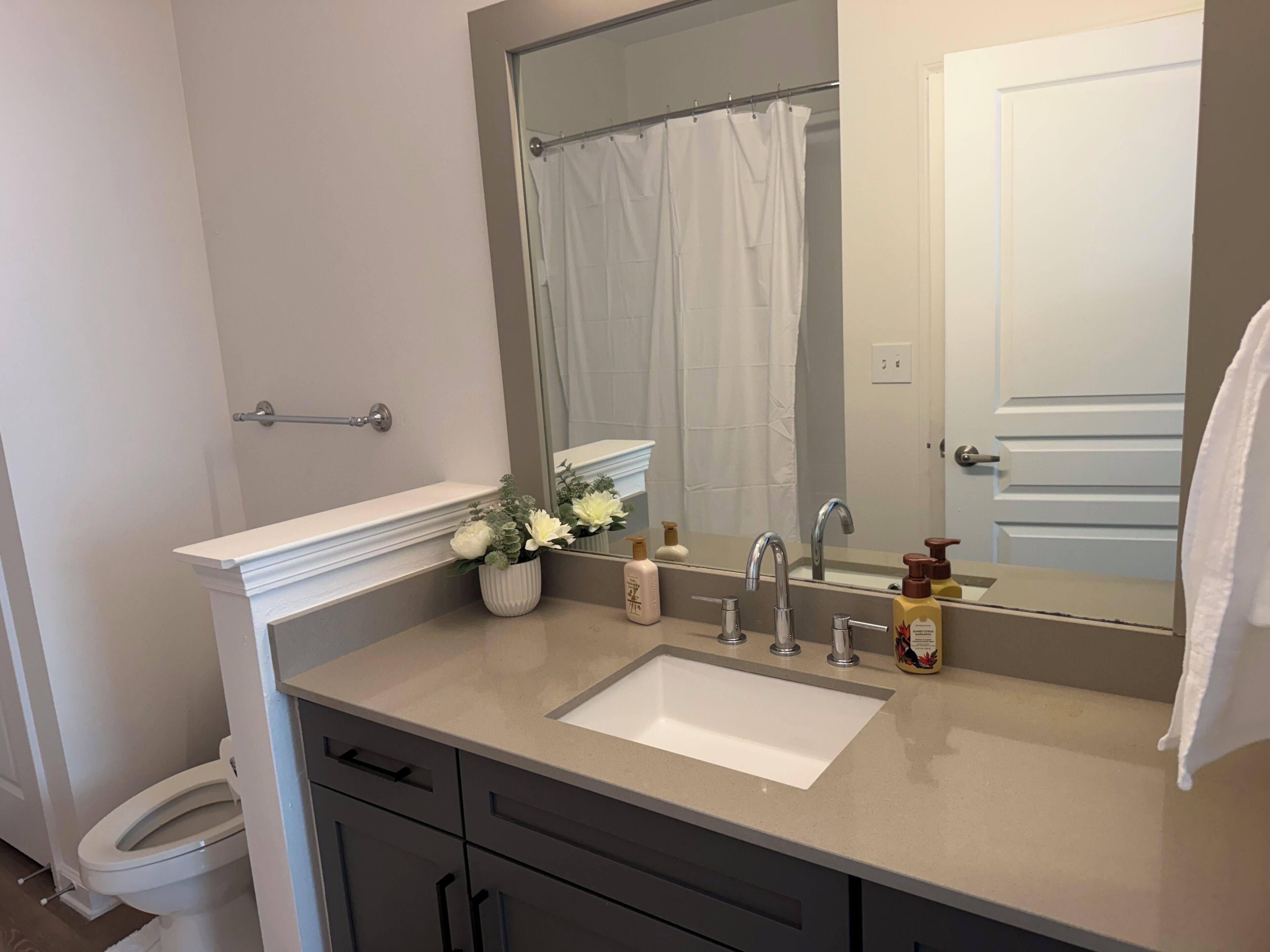 A bathroom with a white sink, a mirror, a shower curtain, and a toilet.