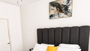 Ein Schlafzimmer mit Bett, Kopfstütze, einem Gemälde und einer Tür.