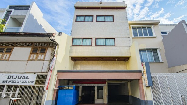 A multi-story building with a flat facade, a ground-level entrance with a red awning, and a blue dumpster outside. - Luxury Twin Stay With Free Wifi and Parking (Makassar)