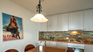 Cozinha com armários brancos, painel de backsplash de pedra, mesa de jantar de madeira com uma tigela de laranjas e luminária pendente.