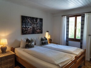 A bedroom with a bed, two nightstands, a wall-mounted lamp, a window with curtains, and a painting of deer. - Berghaus Lichtblick Appartement/Fewo, Bad, WC, 12-Bettwohnung by Interhome (Arosa)