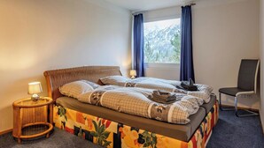 Une chambre à coucher comprenant un lit, une chaise, une table de chevet, une fenêtre avec des rideaux et une vue sur les arbres.