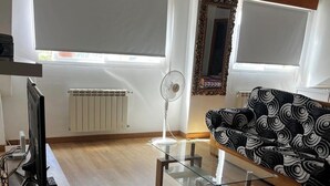 Een woonkamer met een glazen salontafel, een bank met een gestreept hoesje, een televisie op een dressoir en een radiator.