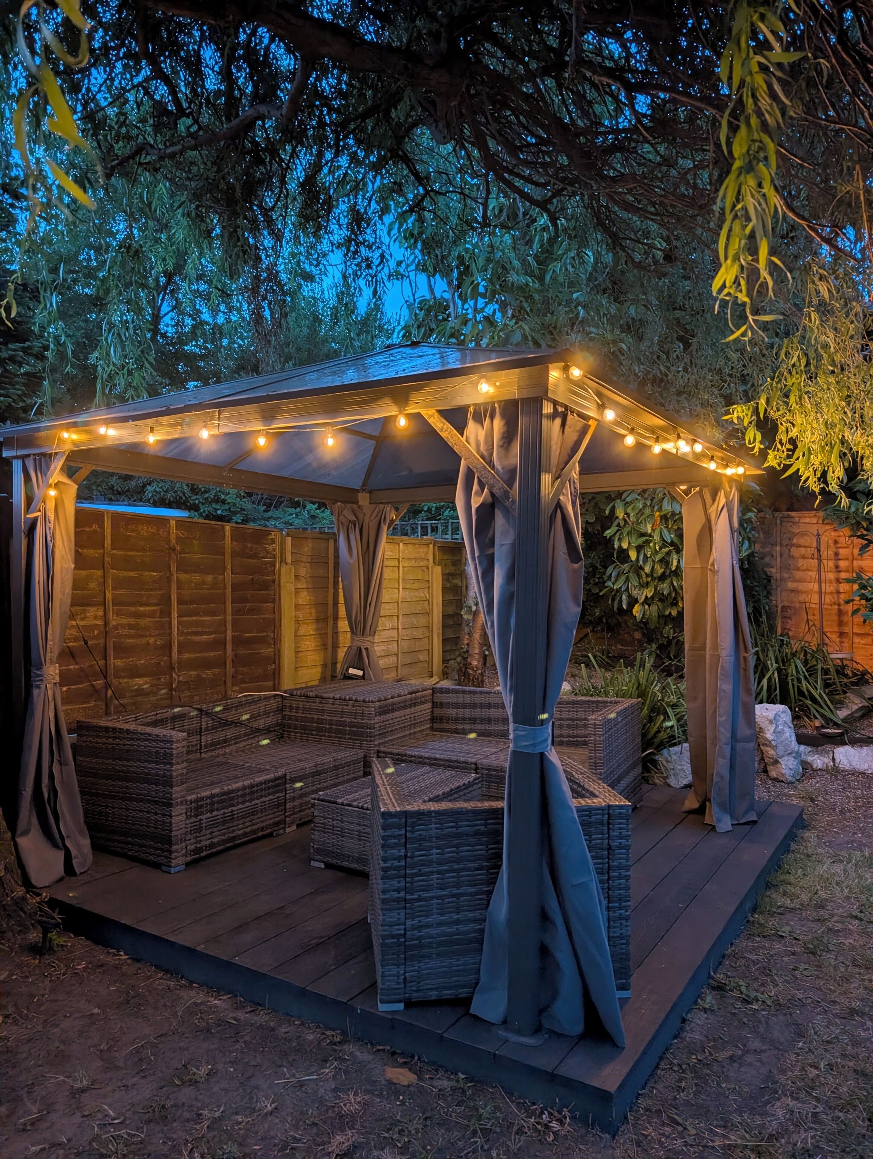 A covered outdoor seating area with string lights, wicker furniture, and curtains.