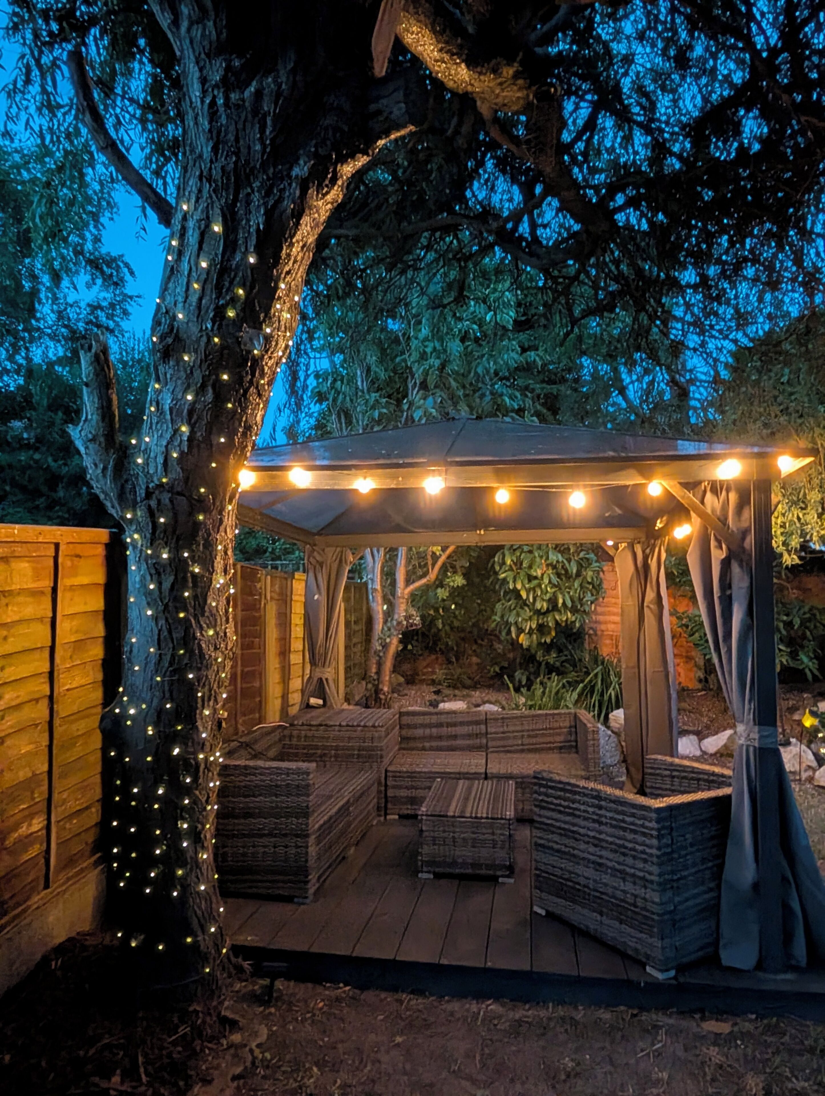 A wooden deck with a pergola, string lights, and outdoor furniture.