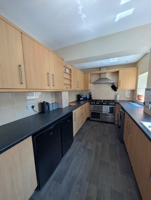 A modern kitchen with wooden cabinets, a black countertop, a built-in oven, and a dishwasher. - Seaside Retreat - Golf Coast & Holiday Home  (Southport)