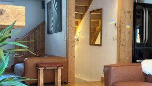 Un soggiorno moderno con una scala in legno, un divano in pelle, una panca in legno e un frigorifero nero.