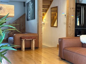 Ein modernes Wohnzimmer mit einer Holztreppe, einem Ledersofa, einer Holzbank und einem schwarzen Kühlschrank.