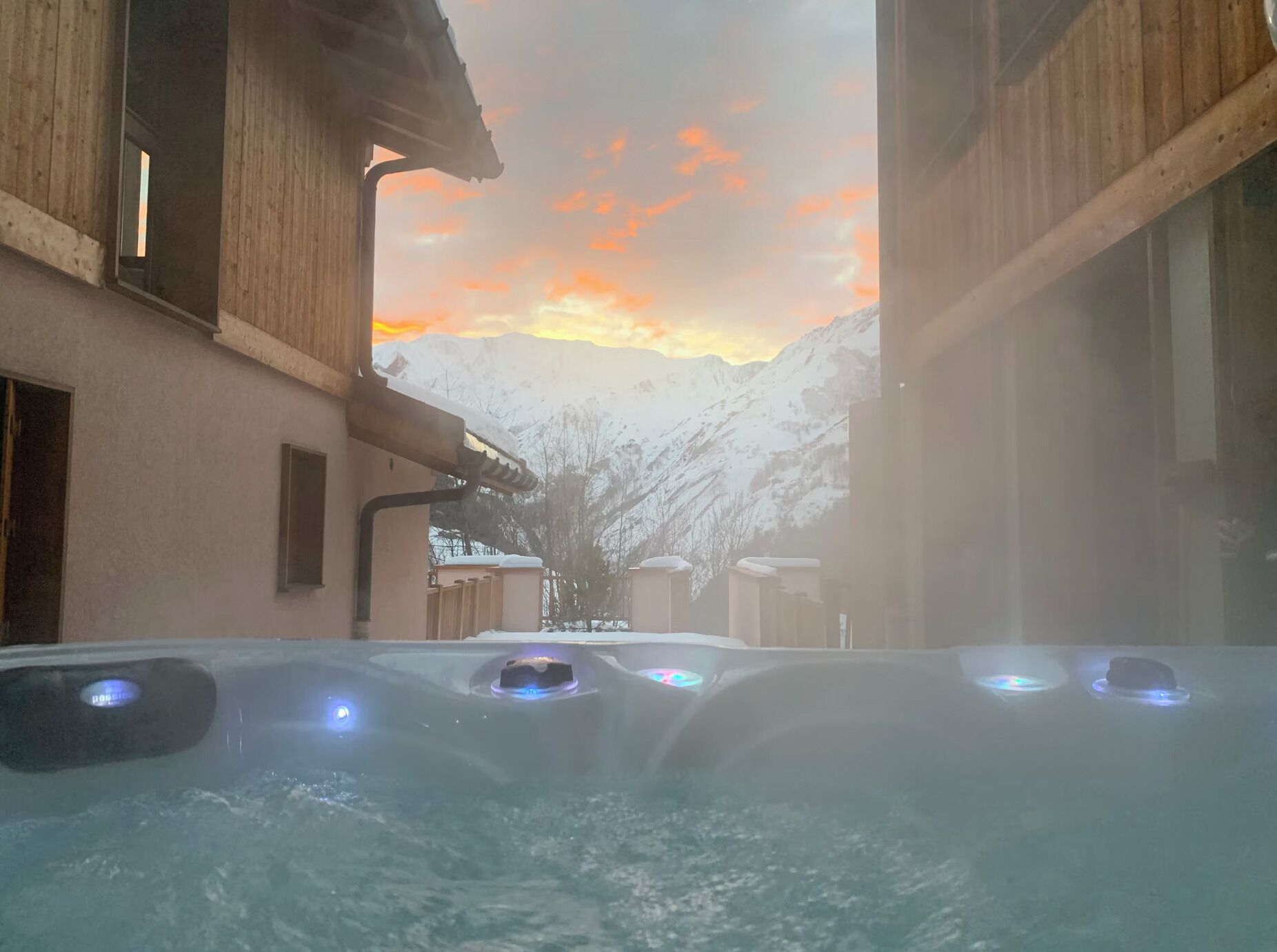 A hot tub with a view of snow-covered mountains and a sunset.