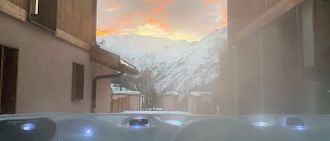 Un jacuzzi con vistas a montañas nevadas y un atardecer.