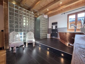 A modern interior with a wooden ceiling, dark flooring, and a seating area with ornate chairs.