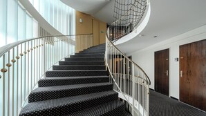 A spiral staircase with black steps and white balusters, leading to a landing with a glass wall and a wooden door. - Alexandra 120 by Arosa Vacations Appartement/Fewo, Dusche und Bad, WC, 2-Bettwoh by Interhome (Arosa)