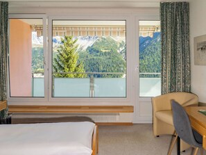 Ein Hotelzimmer mit Bett, Sessel, Tisch und einem großen Fenster mit Blick auf die Berge.