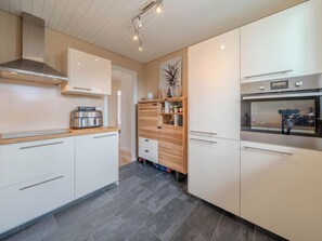 A modern kitchen with white cabinetry, a built-in oven, and a wooden shelf unit. - Viktoria B33 by Arosa Vacations Appartement/Fewo, Dusche und Bad, WC, 2 Schlafrä by Interhome (Arosa)