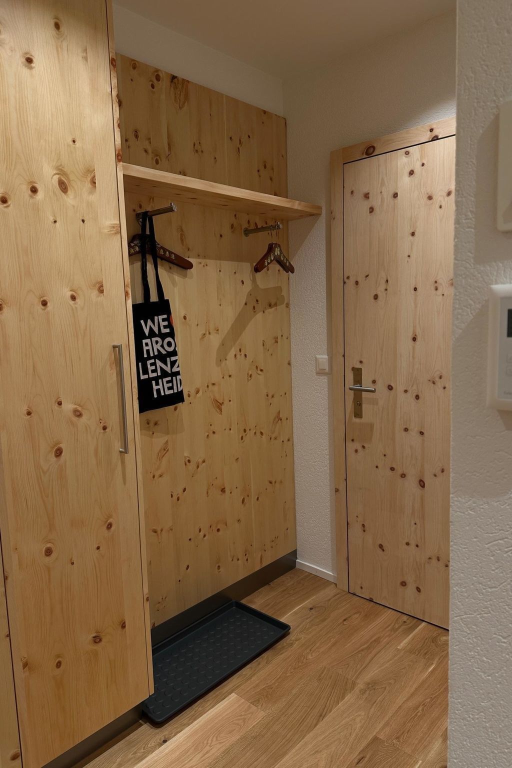 Ein Holzschrank mit einer schwarzen Matte unten, einer Kleiderstange mit Kleidung und einem Schild an der Tür.