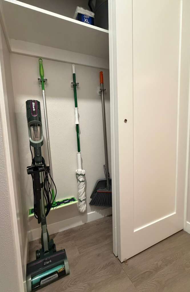 A hallway with a vacuum cleaner, a broom, and a mop on the wall.
