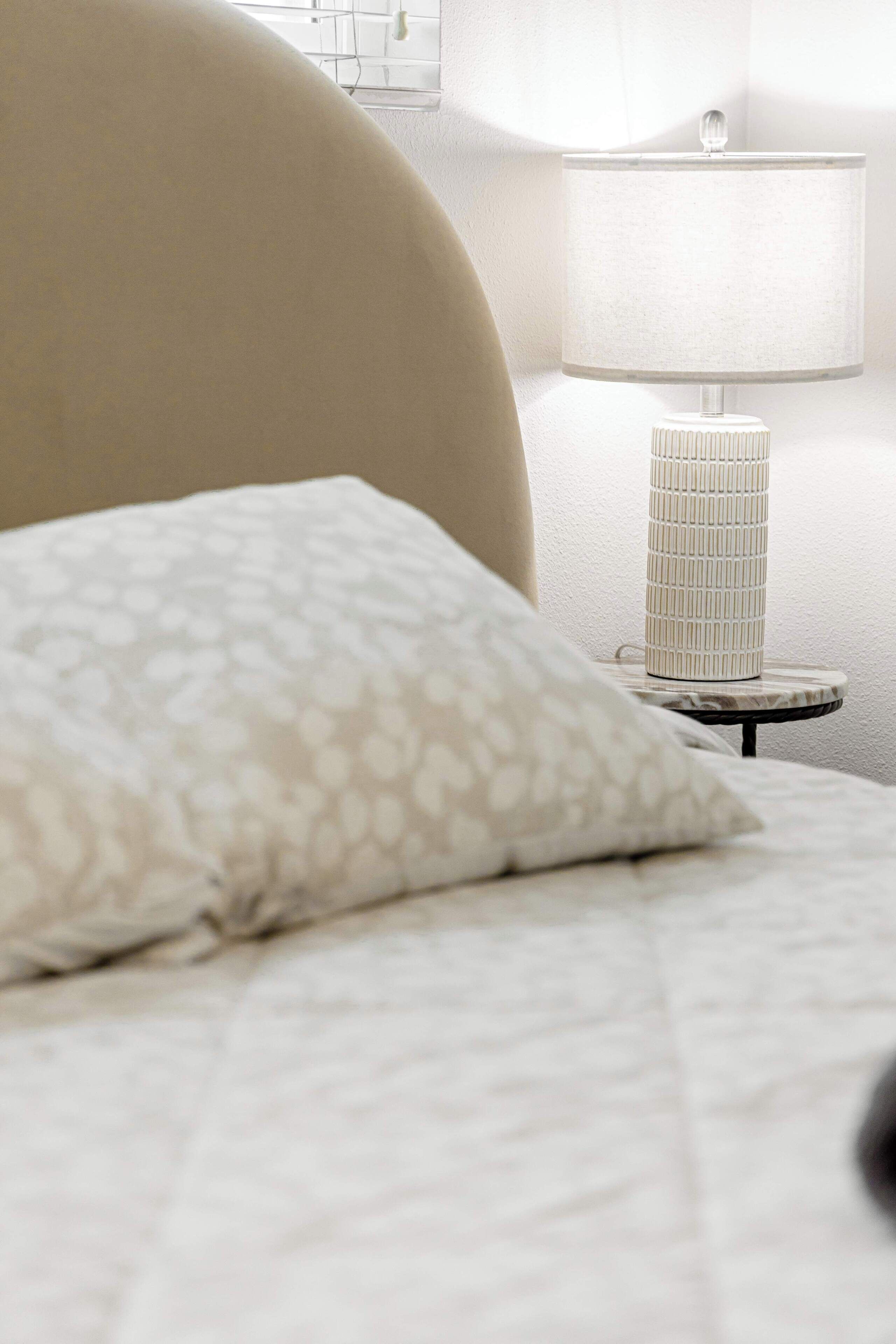 Un lit avec un oreiller à motifs, une lampe de chevet et un luminaire fixé au mur.