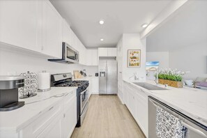 Une cuisine moderne avec des meubles blancs, un réfrigérateur en acier inoxydable, un four à micro-ondes et une cuisinière.