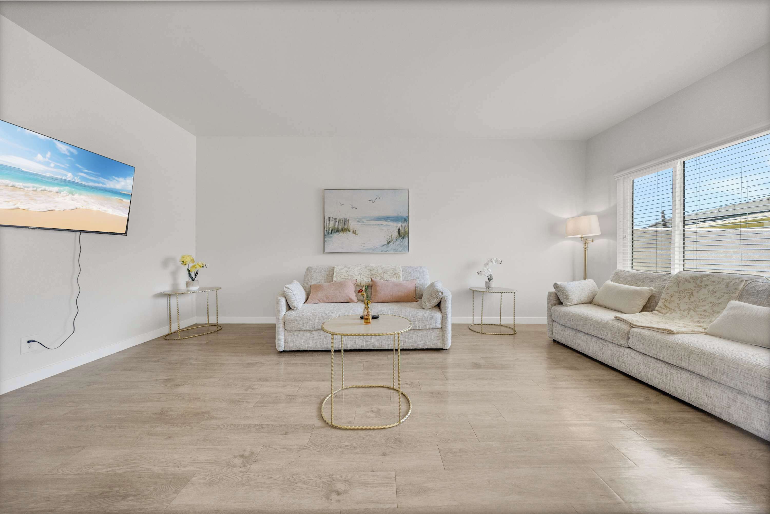 A living room with a sofa, a coffee table, a painting, and a TV mounted on the wall.
