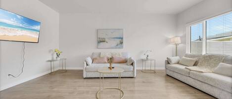 A living room with a sofa, a coffee table, a painting, and a TV mounted on the wall.