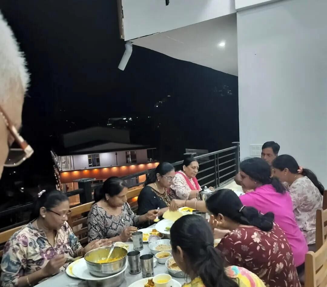 Un grupo de personas cenando en una mesa al aire libre con baranda, en un ambiente moderno y con vista al cielo nocturno.