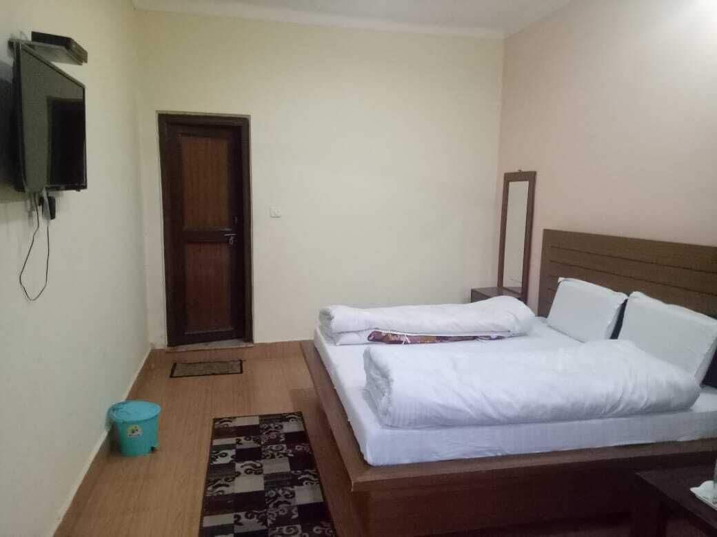 A bedroom with a bed, a television mounted on the wall, a door, and a small trash bin.