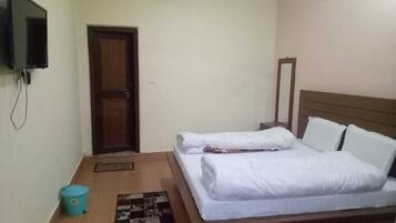 A bedroom with a bed, a television mounted on the wall, a door, and a small trash bin.