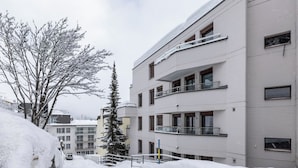 Ein mehrstöckiges Gebäude mit Balkonen, verschneiter Erde und blauem Himmel.