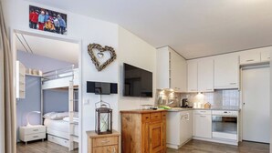 Eine moderne Küche mit weißen Schränken, einem Holzschrank, einem an der Wand montierten Fernseher und einem Holzboden.