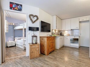 A modern kitchen with white cabinets, a wooden cabinet, a TV mounted on the wall, and a wooden floor. - Haus Lorez B-5 Appartement/Fewo, Dusche oder Bad, WC, 2-Bettwohnung by Interhome (Arosa)