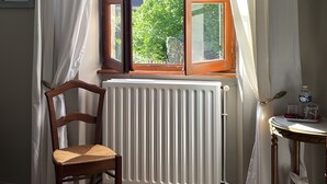 A room with a wooden chair, a radiator, a window with curtains, a small table with a bottle, and a picture frame on the wall. - Bed and Breakfast 'La Chambre JP À "Parenthèse"' with Mountain View, Shared Garden and Wi-Fi (Folles)
