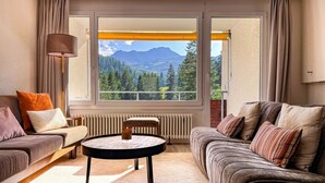 A living room with two sofas, a round coffee table, and a view of mountains through large windows. - Rothornblick 25 by Arosa Holiday Appartement/Fewo, Bad, WC, 4-Bettwohnung by Interhome (Arosa)