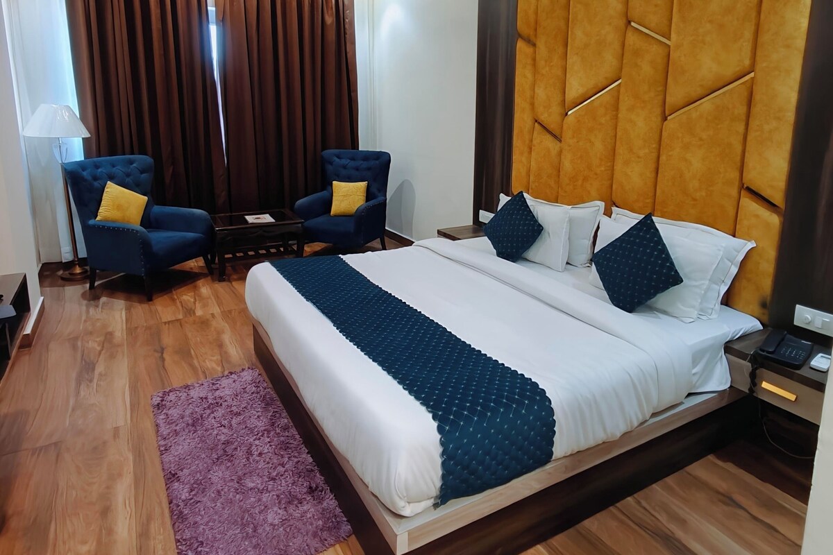 A hotel room with a bed, two armchairs, a ceiling fan, and a wooden floor.