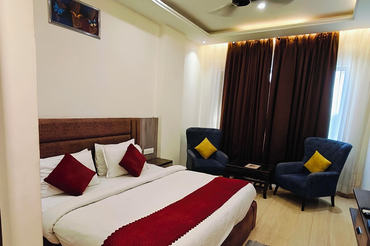 A hotel room with a bed, two armchairs, a ceiling fan, and a window with curtains.
