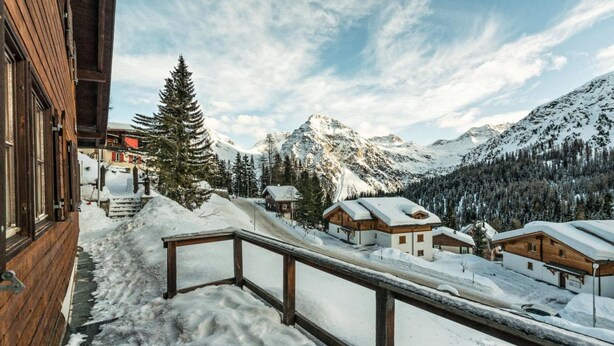 Ein verschneites Bergdorf mit Holzhäusern und einem Holzbalkon.