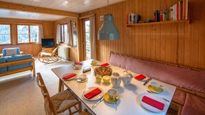 Ein gemütliches Blockhaushaus-Interieur mit Esstisch für zwei Personen, einem Fernseher, Holzwänden und einem Bücherregal.
