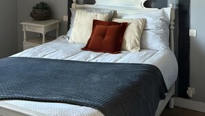 Een slaapkamer met een bed, nachtkastjes, een hanglamp en een raam met gordijnen.